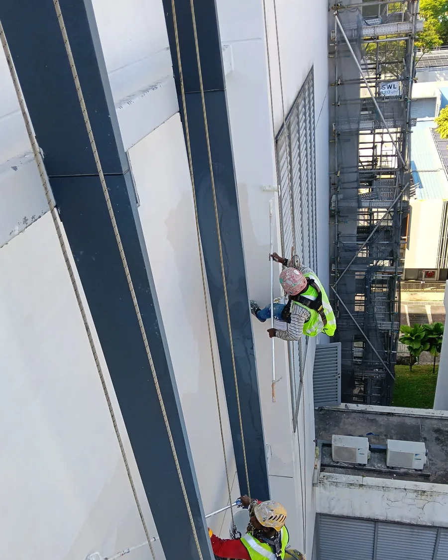 Rope-access painter applying exterior sealer to a high-rise elevation