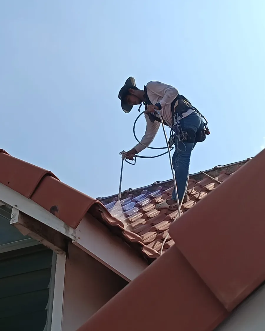 Painter spray-applying protective roof coating across clay roof tiles